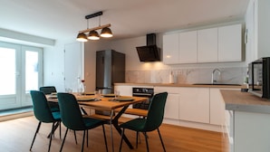 Une cuisine moderne avec des meubles blancs, un plan de travail en bois et un coin repas avec des chaises vertes.