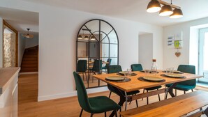 Un coin repas avec une table en bois, des chaises vertes et un grand miroir au mur.