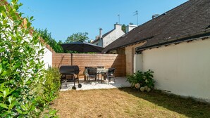 Un jardin avec un espace barbecue, une table et des chaises, et une clôture en bois.