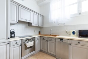 A modern kitchen with white cabinetry, stainless steel appliances, and a window with sheer curtains. - Happyfew La Promenade 53 (Nice)