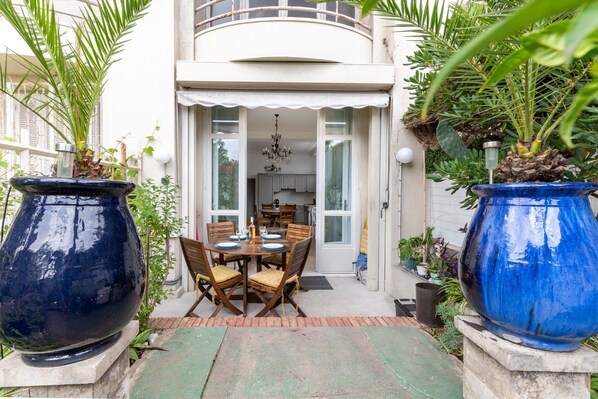 A patio with a dining table and chairs, surrounded by large planters and a view into a house. - Happyfew La Promenade 53 (Nice)