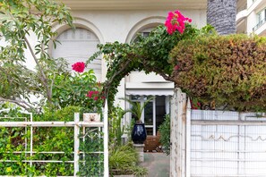 A garden entrance with a white gate, a wooden bench, and a potted plant.