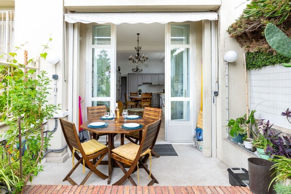 A patio with a wooden table and chairs, surrounded by potted plants and a cactus.