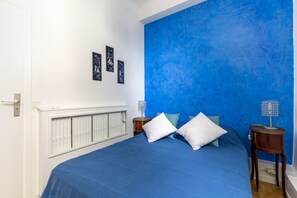 A bedroom with a blue bedspread, white pillows, and a blue accent wall. There are three framed pictures on the wall.