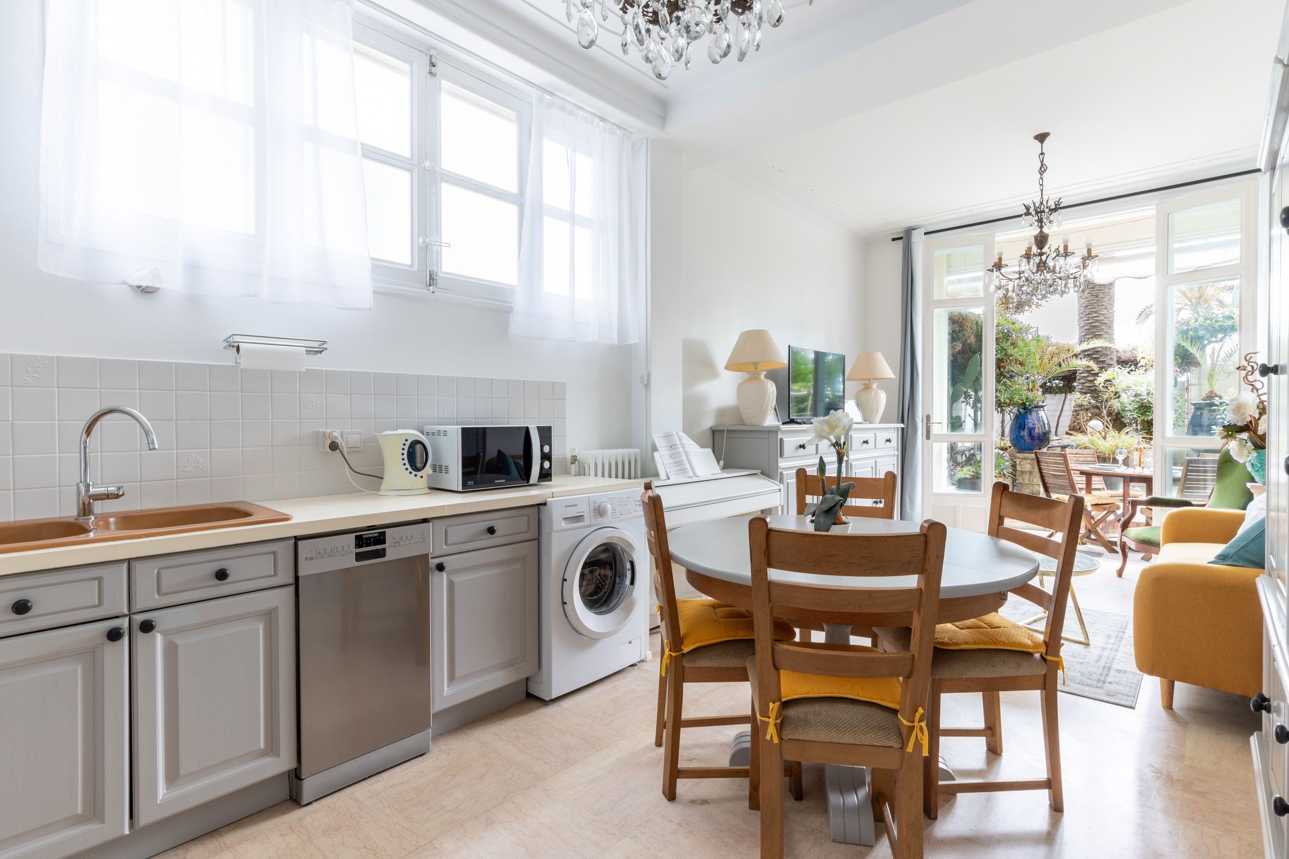 A modern kitchen with a dishwasher, microwave, and washing machine. There is a dining area with wooden chairs and a table.