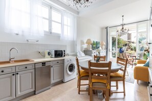 A modern kitchen with a dishwasher, microwave, and washing machine. There is a dining area with wooden chairs and a table.