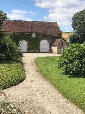 Un bâtiment avec un chemin de gravier menant à une porte blanche, entouré de verdure et sous un ciel dégagé.