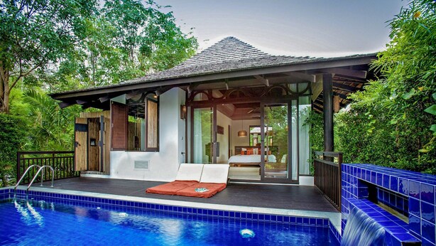 Un espace aménagé au bord de la piscine, comprenant un coin salon couvert, une chaise longue et une petite cascade décorative.