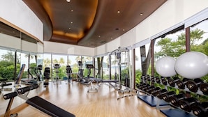 Une salle de sport moderne équipée de divers appareils d’exercice, dotée de grandes fenêtres et offrant une vue sur la verdure.