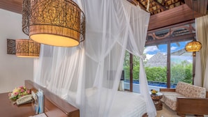 Une chambre à coucher avec un lit à baldaquin, un bureau en bois avec un téléphone et des papiers, une petite table ronde avec un panier de fruits et un canapé.