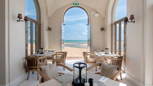 A dining area with tables and chairs, large windows with beach views, and a glass enclosure.