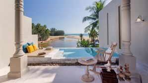 A poolside area with a view of the beach and palm trees, a wooden chair, a table with a chess set, and decorative vases.