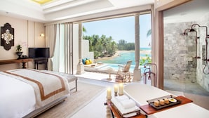 A hotel room with a bed, a sitting area with a view of the beach, a bathtub, and a shower area.