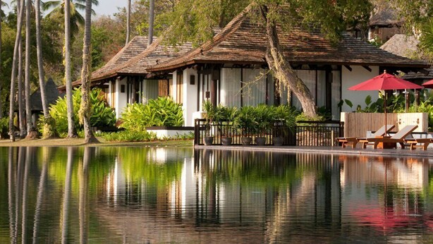 A traditional building with a thatched roof, surrounded by lush greenery and a calm reflective pool. - The Vijitt Resort - Deluxe Beachfront Villa (Rawai)