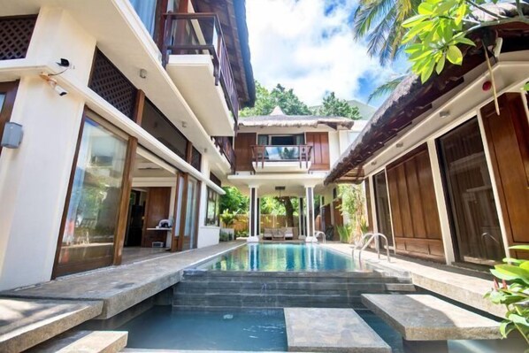 Un área de piscina moderna con escalones que bajan al agua, rodeada de edificios con ventanas amplias y balcones.