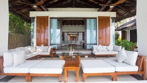 A covered outdoor seating area with wooden furniture and a glass table, leading to a modern interior space. - Harlan Beach Villa Boracay (Boracay Island)