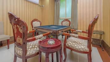 A pool table with four chairs, a small table, and a window with curtains.