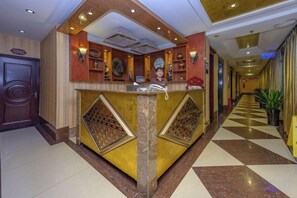 A hotel reception area with a check-in counter, a reception desk, and a checkered floor pattern.