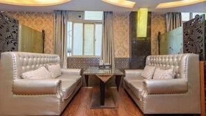 A room with two leather sofas facing a glass table, wooden flooring, patterned wallpaper, and a window with curtains. - Quxian Century Sunshine Hotel-The West Hotel (Qu County)