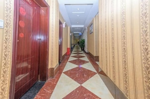 Un pasillo de hotel con paredes estampadas, suelo de cuadros y una puerta con un emblema circular.