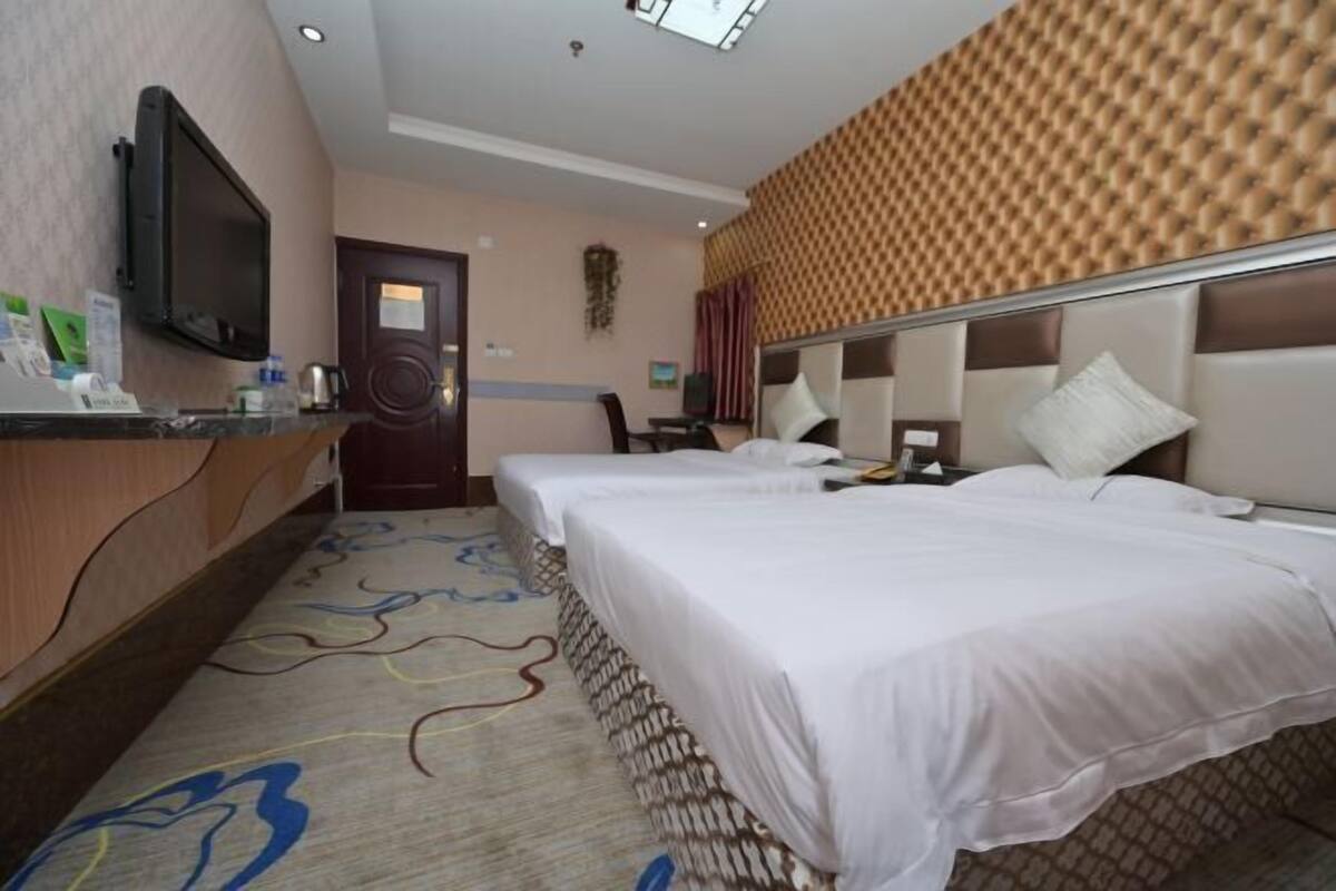 Ein Hotelzimmer mit zwei Betten, einem Fernseher, einem Schreibtisch mit Computer und einem gemusterten Teppich.