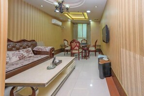 A living room with a sofa, dining table, chairs, and a TV mounted on the wall.
