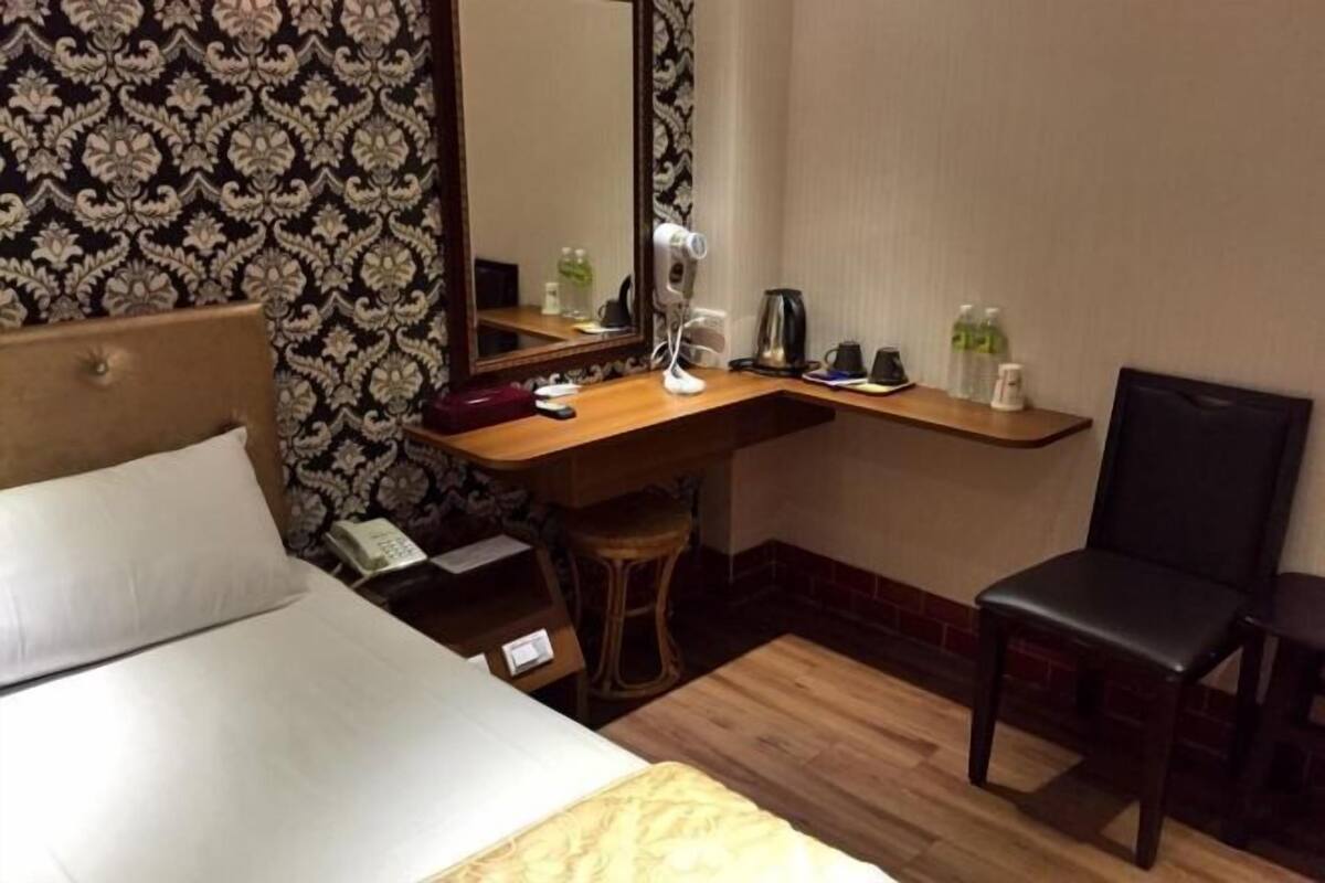 Een hotelkamer met een bed, een bureau met spiegel, een stoel, een telefoon en een klein krukje.