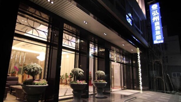 L’entrée d’un hôtel, agrémentée de grands pots de plantes, dotée d’une façade moderne et d’une enseigne bien visible.
