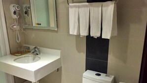 Une salle de bain avec un lavabo blanc, un miroir, un porte-serviettes, des toilettes et un panier.