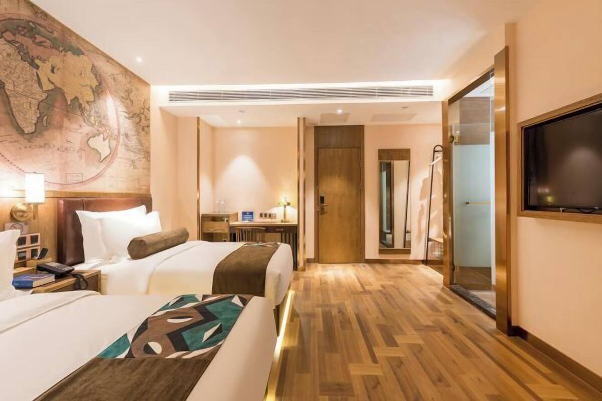 Habitación de hotel con dos camas, un escritorio, un mapa en la pared, un televisor y zona de ducha.