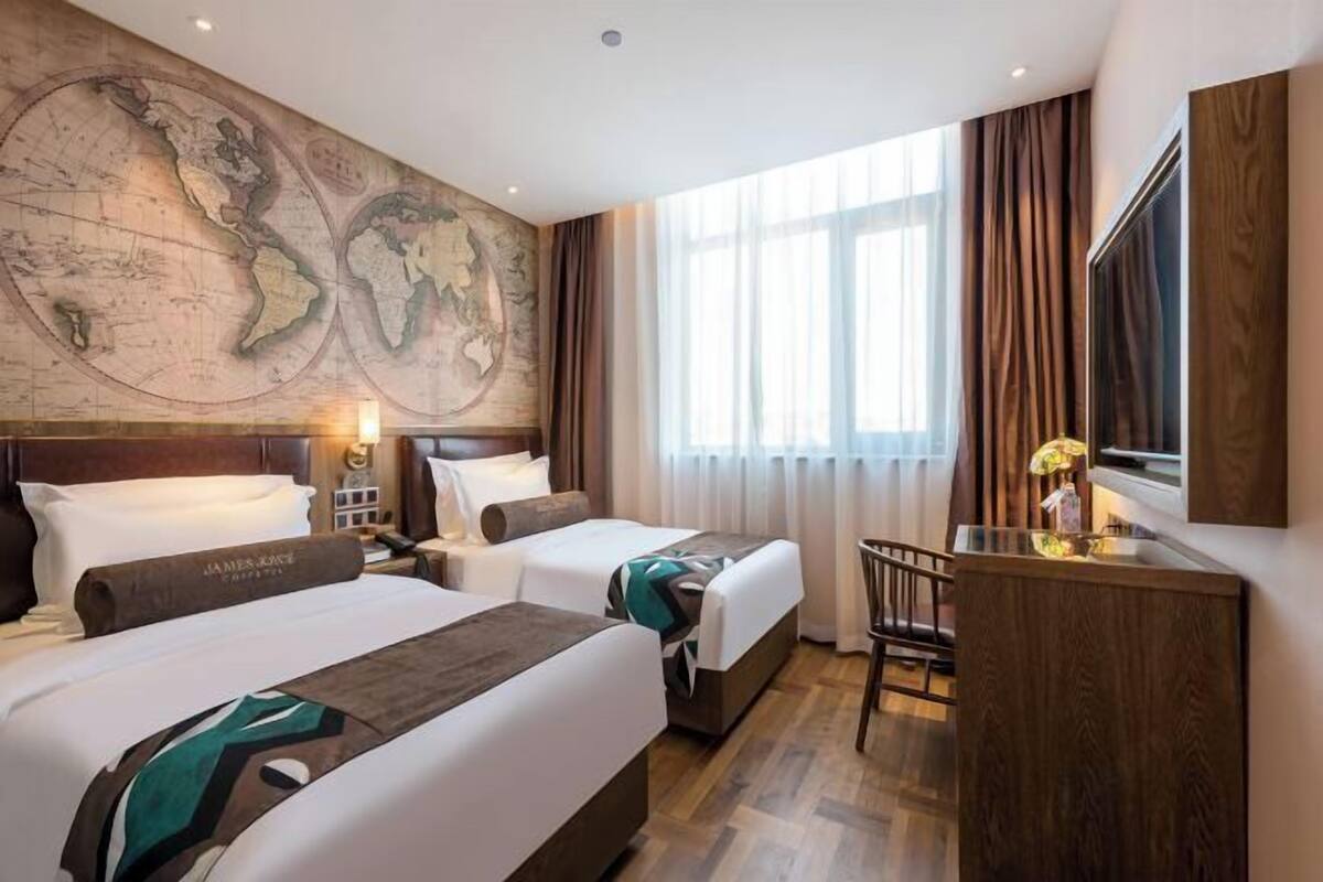 Habitación de hotel con dos camas, un escritorio, una silla, un gran mapa mundial en la pared y una ventana con cortinas.