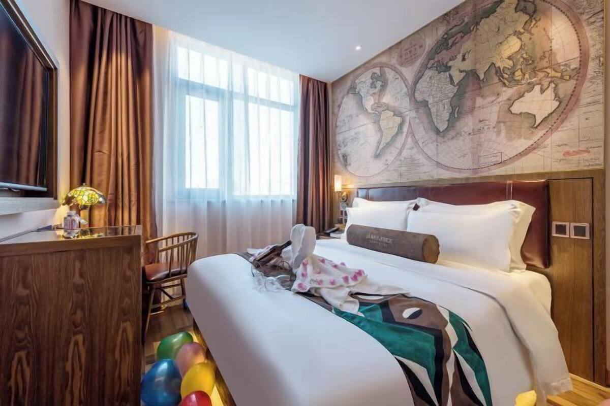Habitación de hotel con una cama grande, un escritorio con lámpara, una silla, un mapa en la pared y una ventana con cortinas.