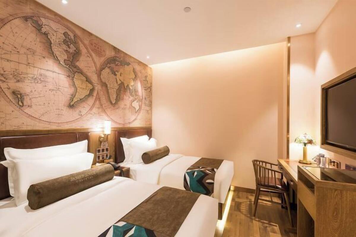 Habitación de hotel con dos camas, un escritorio, una silla, un televisor y un gran mapa mundial en la pared.