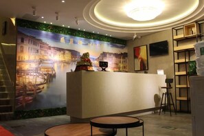 A hotel reception area with a mural, a reception desk, a staircase, and a seating area. - Xinzheng Venice Fashion Hotel (Xinhua Road Zhonghua Road) (Xinzheng)
