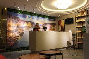 A hotel reception area with a mural, a reception desk, a staircase, and a seating area.