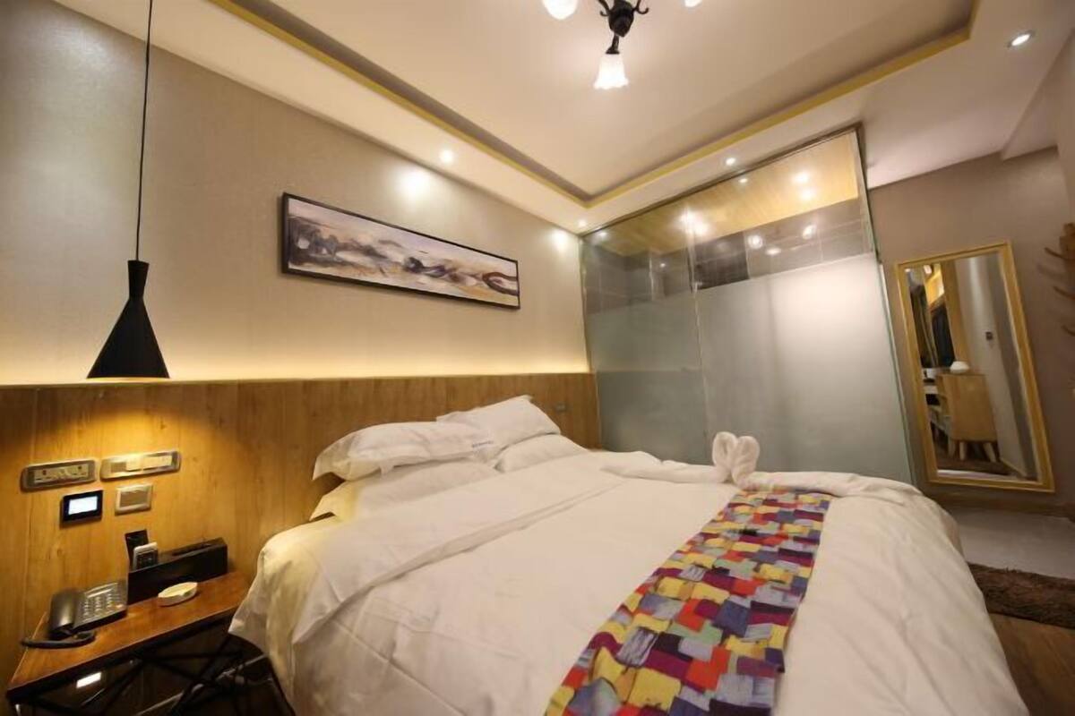 Ein Hotelzimmer mit Bett, Nachttisch, Telefon, Kunstwerk und Spiegel.