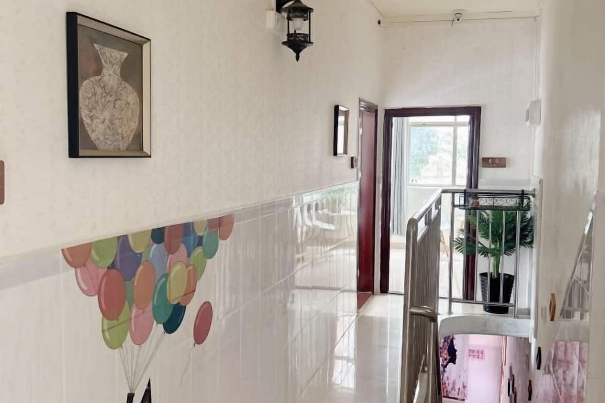 A hallway with a tiled floor, a framed artwork, a wall-mounted light fixture, and a potted plant.