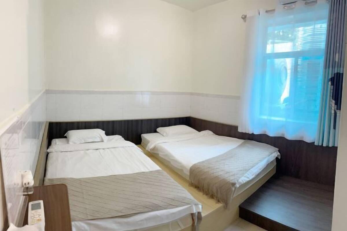 A small hotel room with two single beds, a desk with a chair, and a window with curtains.