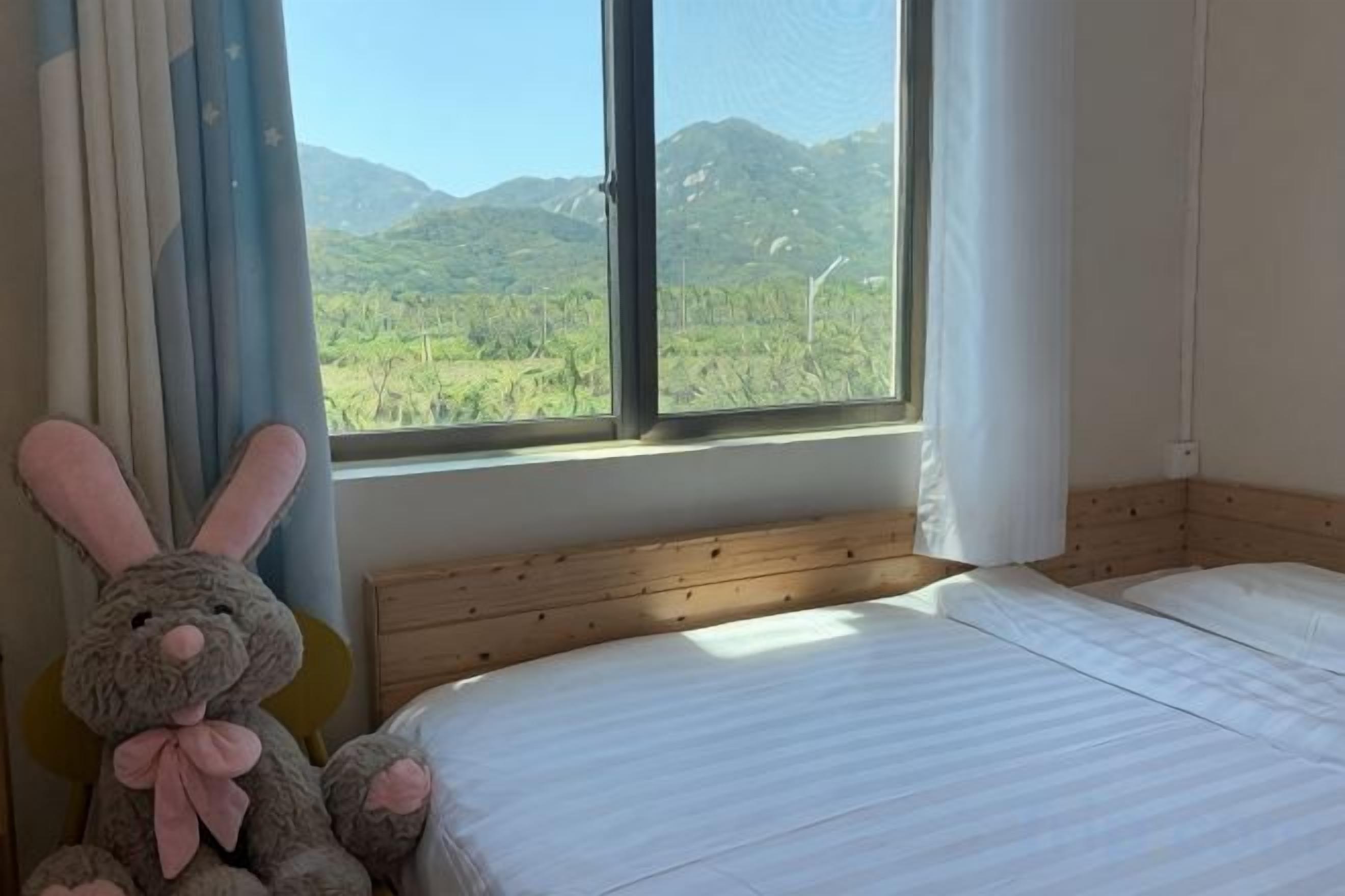 A bedroom with a bed, a window with a view of greenery, and a stuffed toy.