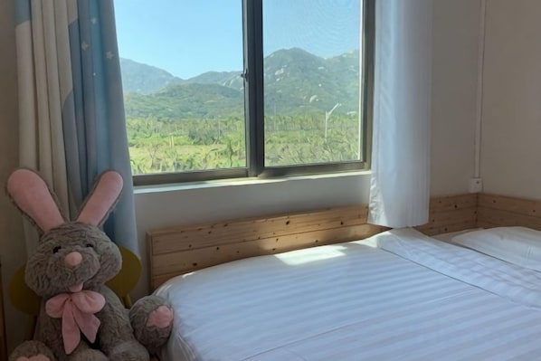 A bedroom with a bed, a window with a view of greenery, and a stuffed toy. - Yingyuge Inn (Shenzhen)