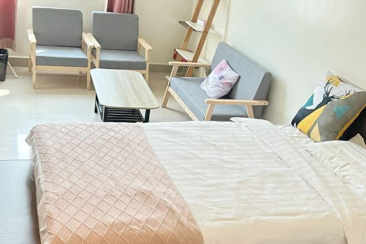 A room with a bed, two grey chairs, a small table, and a sofa with a pillow.