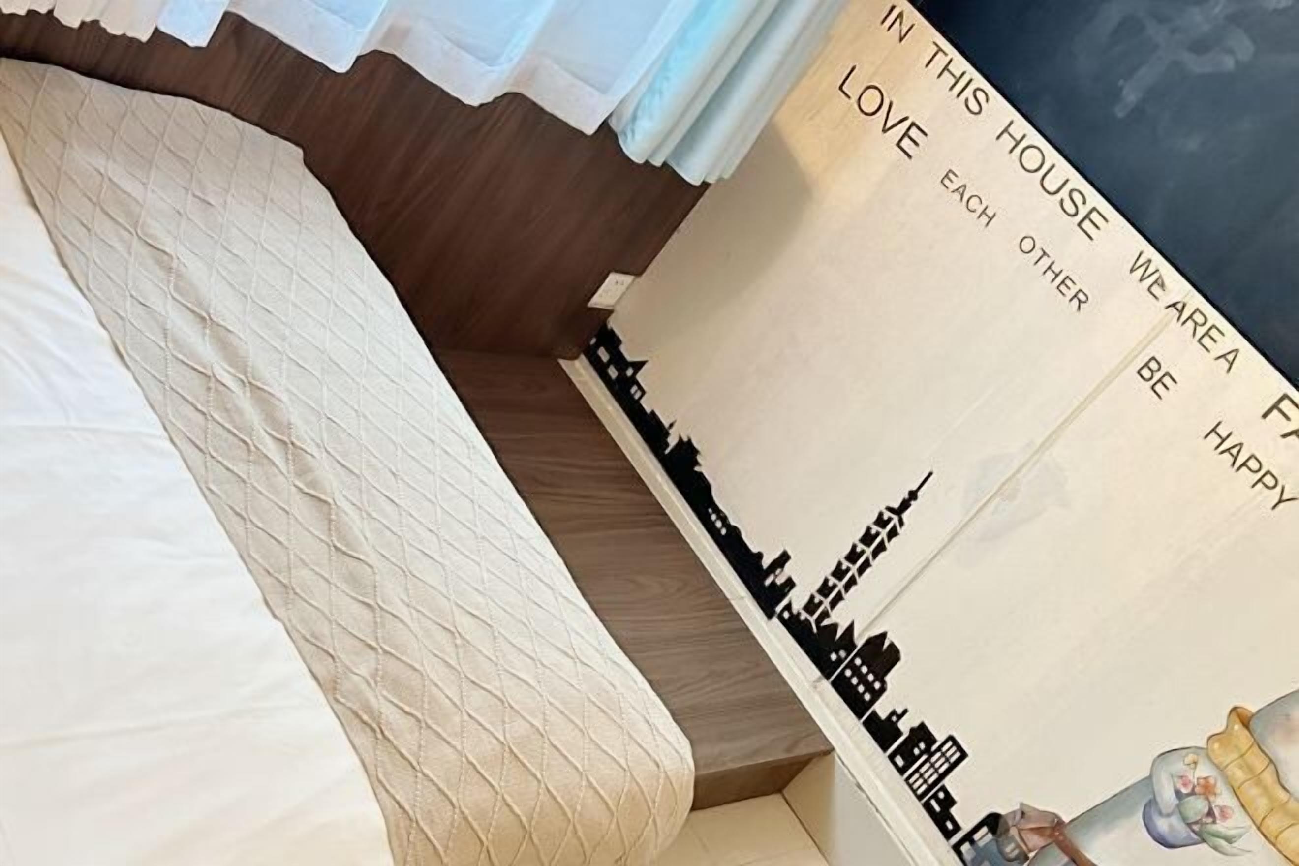 A bed with a quilted headboard, a wall with a cityscape mural, and a partial view of a window with curtains.