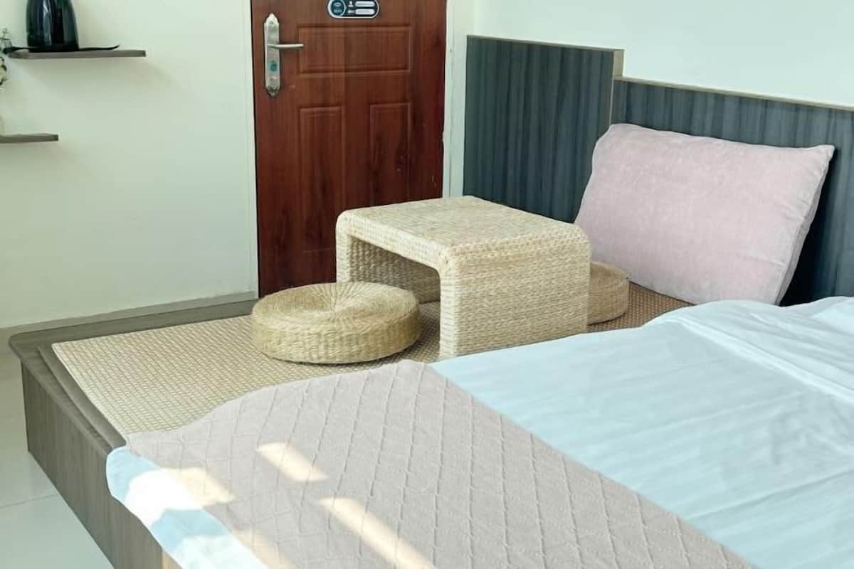 A bed with a headboard, a bedside table, a small stool, and a wall-mounted shelf.