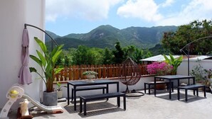 Une terrasse avec une table et des chaises, une balançoire et une vue sur les montagnes.