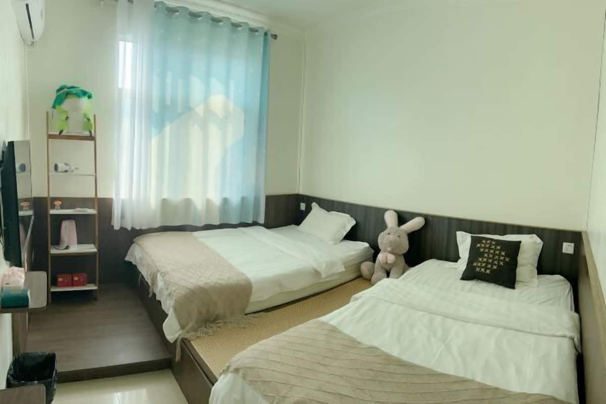 A hotel room with two beds, a wardrobe, a desk with a chair, and a window with curtains.