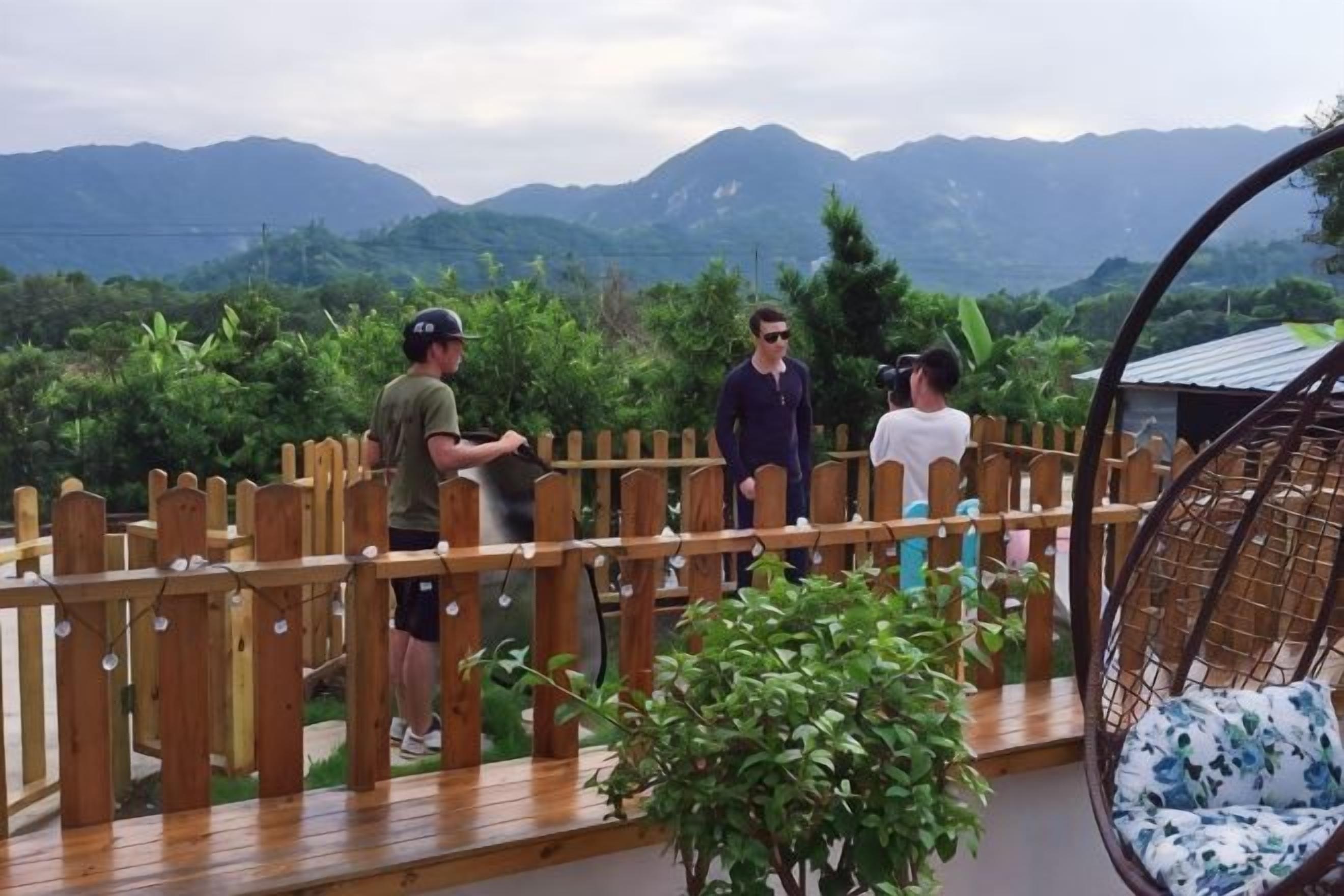Una terraza de madera con vistas a montañas, una silla colgante y una valla de madera.