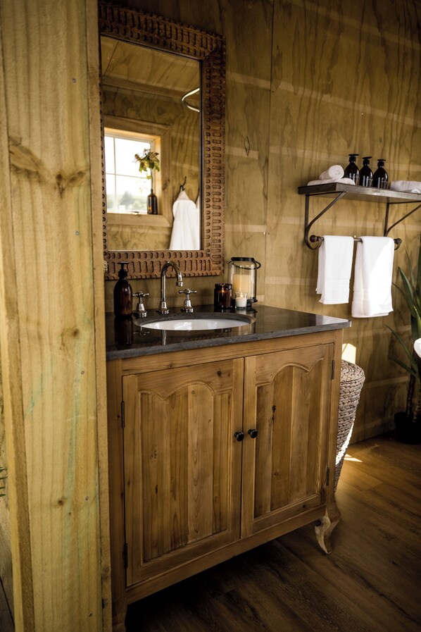 Un baño de madera con lavamanos, espejo y repisas con artículos de aseo.
