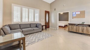 Un salon spacieux avec un canapé gris, une table basse en verre et un tapis à motifs.