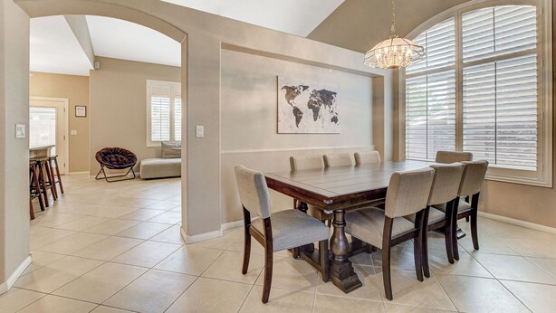 Un coin repas avec une grande table et des chaises, une carte du monde accrochée au mur et une fenêtre avec des stores.