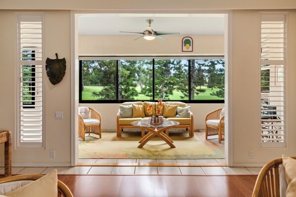 A room with a large window, a ceiling fan, and a sofa with cushions.